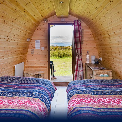 Two Scandinavian dressed beds in a Glamping Pod with a view of the hills through the open front door