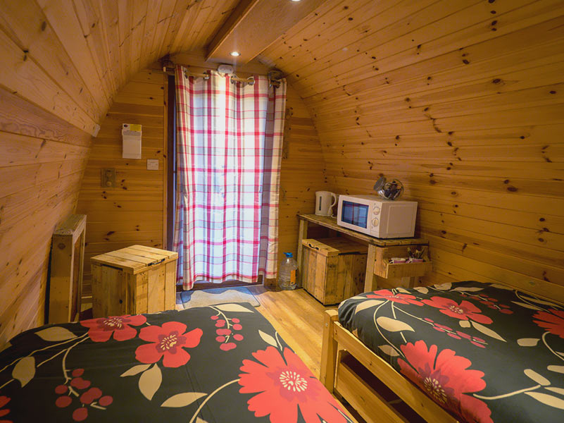 Two floral dressed beds in a Glamping Pod with the door close and the lights on looking cosy