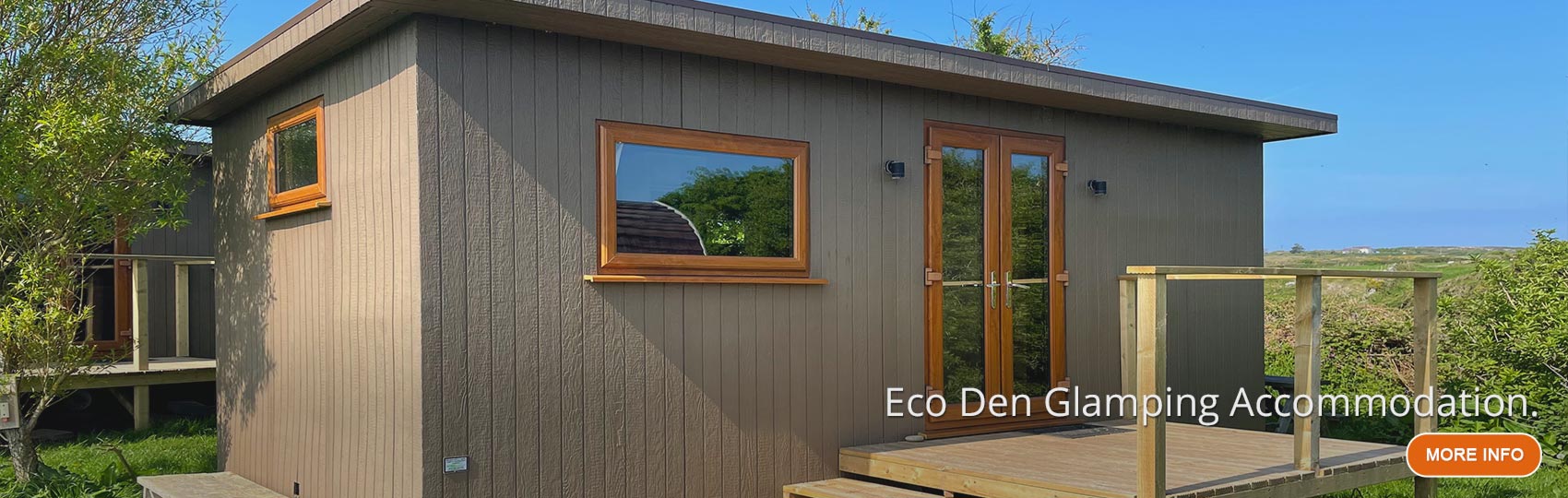 Eco Den with front doors open on the grass with Anglesey Outdoors Main Centre in the background