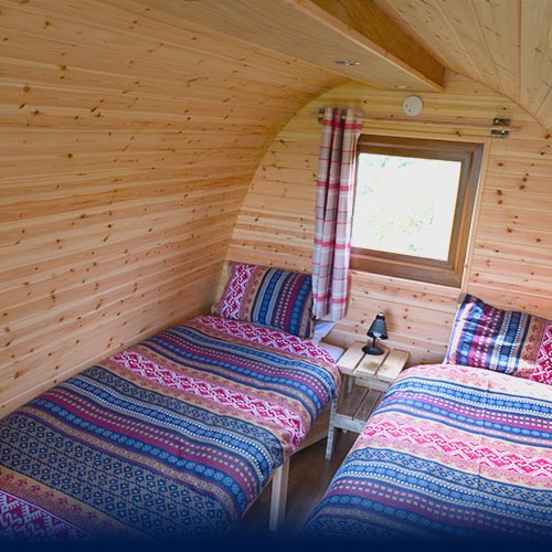 Two Scandinavian dressed beds inside Glamping Pod with porthole window above